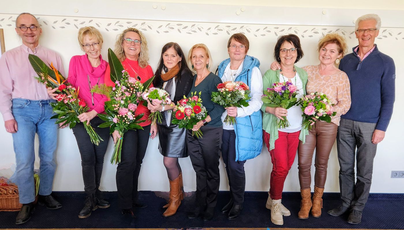 Neun Vereinsmitglieder nebeneinander vor einer hellen Wand, jede und jeder mit einem Blumenstrauß