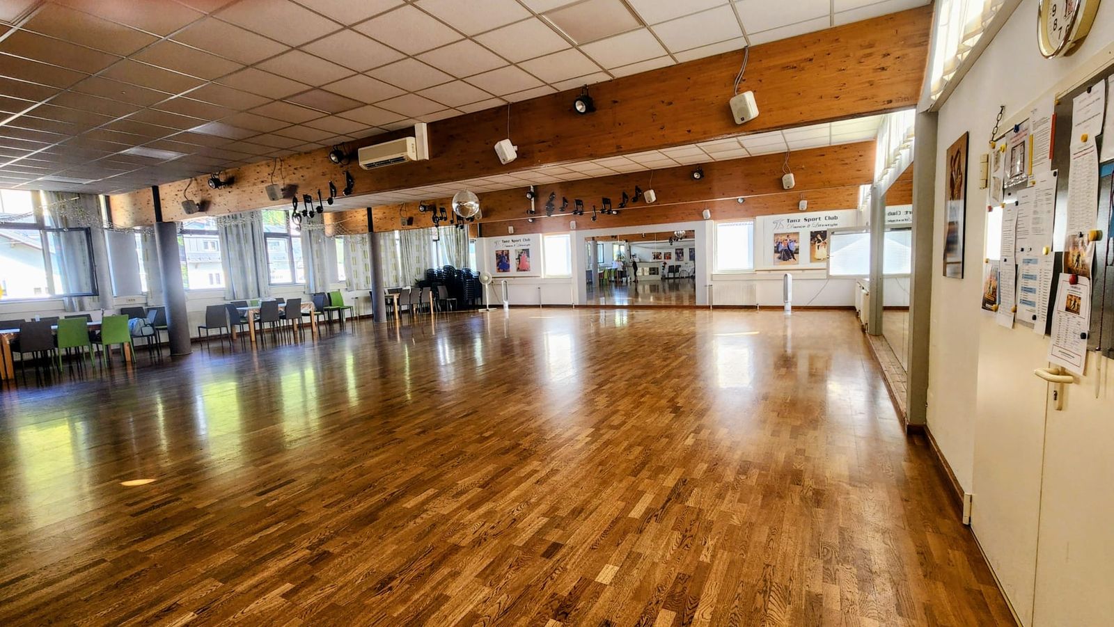 Der große Saal ohne Menschen: weite, glänzende Parkettfläche, links Tische und Stühle vor der Fensterfront, hinten eine Spiegelwand, an der Decke Holzbalken mit Scheinwerfern und Notenschmuck